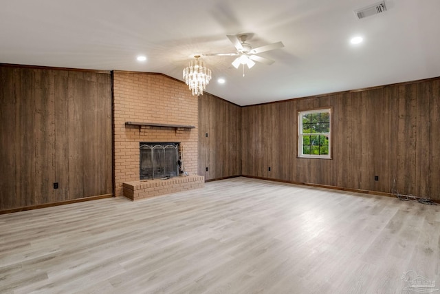 unfurnished living room with wooden walls, ceiling fan with notable chandelier, light wood-type flooring, and a brick fireplace