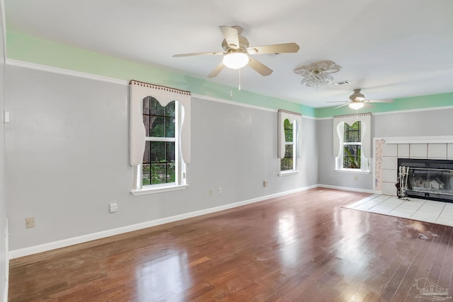 unfurnished living room with light wood-type flooring, a tiled fireplace, and ceiling fan