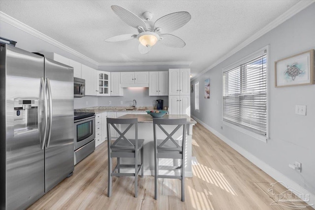 kitchen with a center island, ornamental molding, appliances with stainless steel finishes, a kitchen bar, and white cabinetry