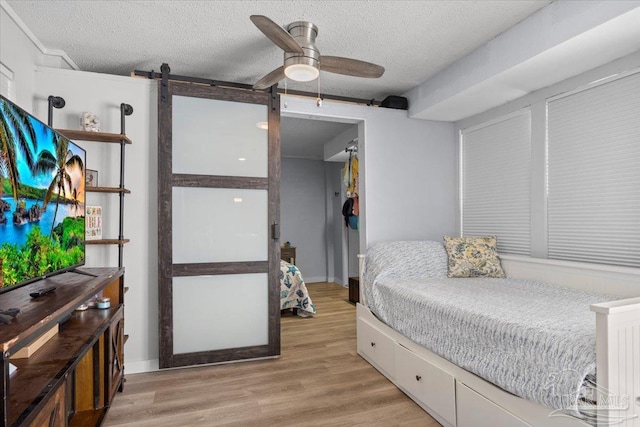 bedroom with light wood-type flooring, a textured ceiling, a barn door, and ceiling fan