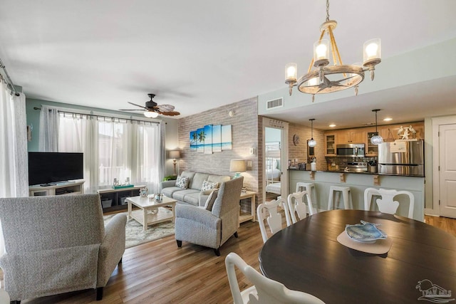 dining room featuring ceiling fan with notable chandelier and light hardwood / wood-style flooring