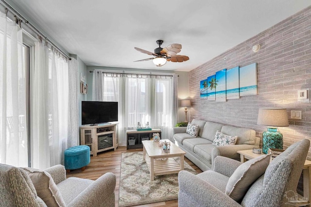 living room with ceiling fan, light hardwood / wood-style floors, and brick wall