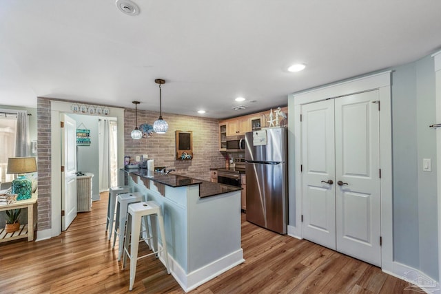 kitchen with pendant lighting, a breakfast bar area, light wood-type flooring, kitchen peninsula, and stainless steel appliances