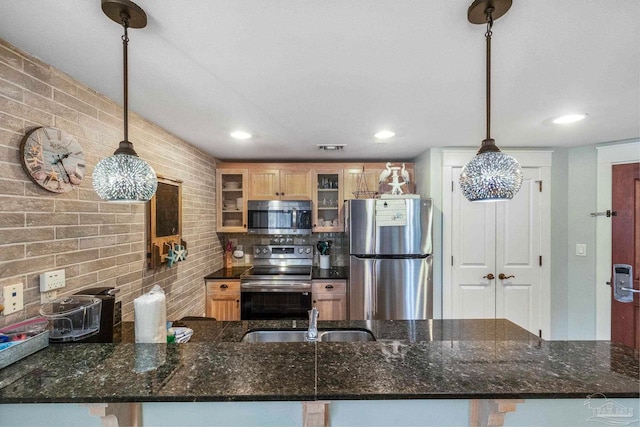 kitchen featuring dark stone countertops, sink, stainless steel appliances, and decorative light fixtures