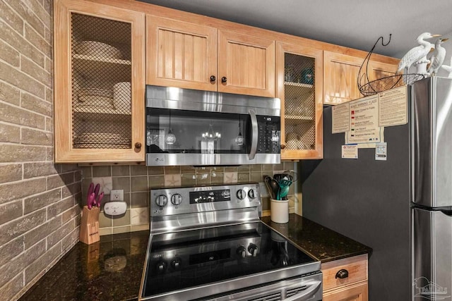 kitchen with dark stone countertops, decorative backsplash, stainless steel appliances, and brick wall