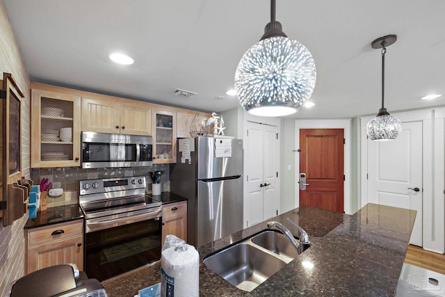 kitchen with dark stone counters, pendant lighting, stainless steel appliances, and sink