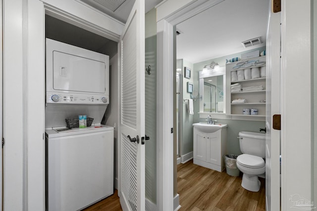 bathroom featuring wood-type flooring, toilet, stacked washer and clothes dryer, and sink