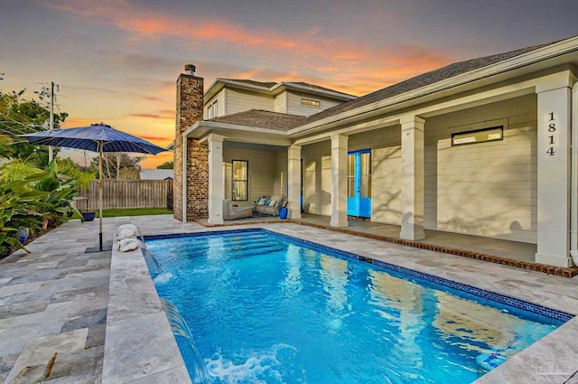 pool at dusk featuring pool water feature and a patio