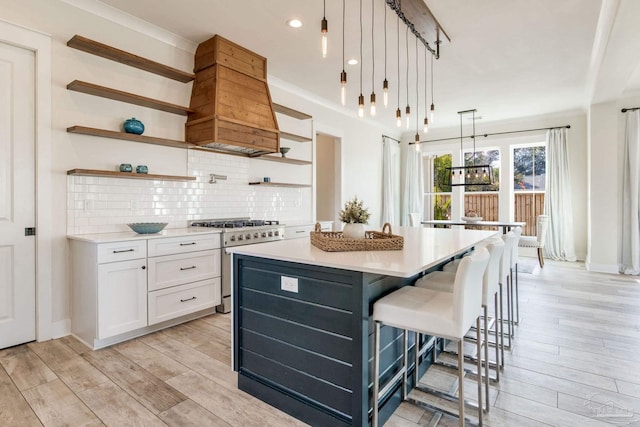 kitchen with high end stove, pendant lighting, light hardwood / wood-style flooring, a center island, and white cabinetry