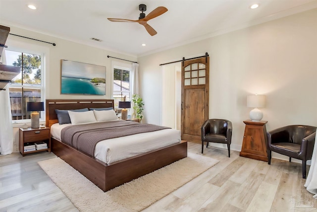 bedroom with ceiling fan, a barn door, light wood-type flooring, and crown molding