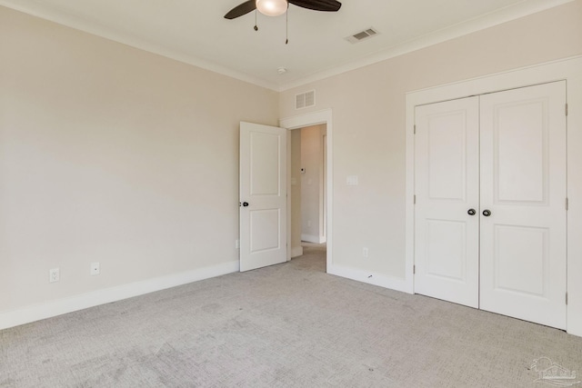 unfurnished bedroom with ceiling fan, light colored carpet, crown molding, and a closet