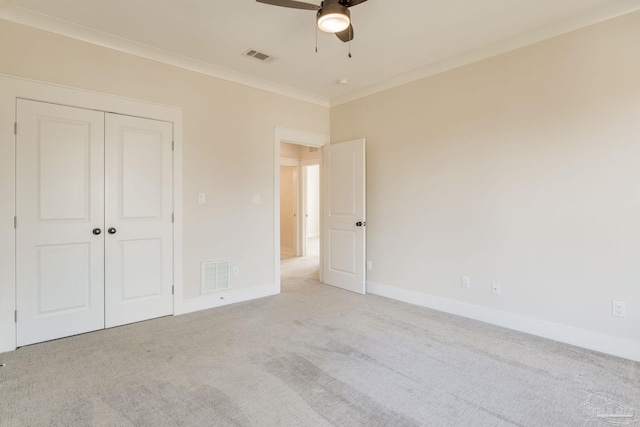 unfurnished bedroom with ceiling fan, light colored carpet, crown molding, and a closet