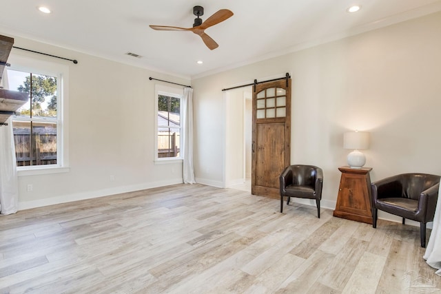 living area featuring light wood-type flooring, a barn door, ceiling fan, and crown molding