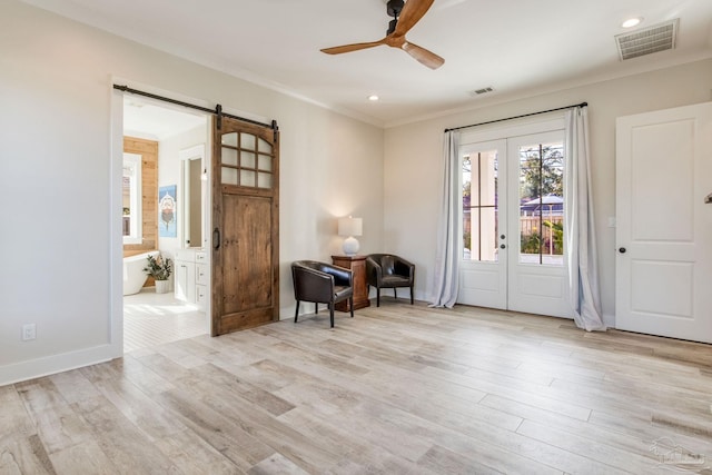 entrance foyer featuring ceiling fan, french doors, a barn door, crown molding, and light hardwood / wood-style floors