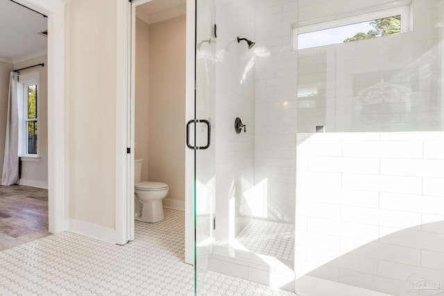 bathroom featuring plenty of natural light, toilet, a shower with door, and ornamental molding