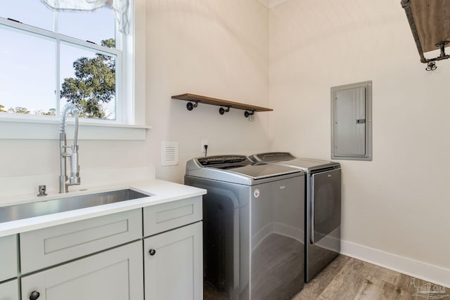 laundry room featuring cabinets, light wood-type flooring, sink, washer and dryer, and electric panel