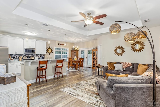 living room featuring ceiling fan, light hardwood / wood-style floors, french doors, and a tray ceiling