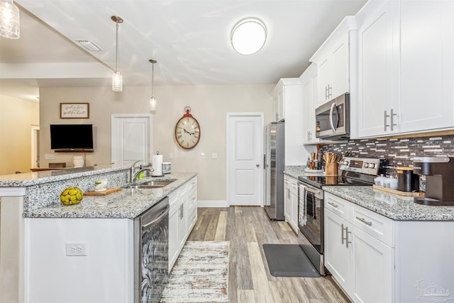 kitchen featuring white cabinetry, sink, stainless steel appliances, pendant lighting, and light wood-type flooring