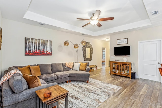 living room with ceiling fan, light wood-type flooring, and a tray ceiling