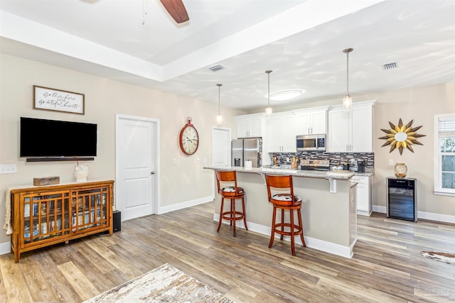 kitchen featuring an island with sink, decorative light fixtures, a breakfast bar area, white cabinets, and appliances with stainless steel finishes