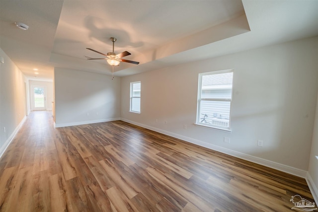 spare room with ceiling fan, a tray ceiling, and wood-type flooring