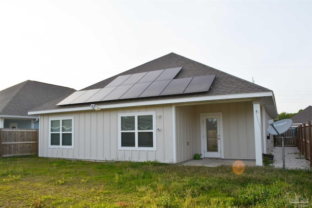 rear view of property with a lawn and solar panels