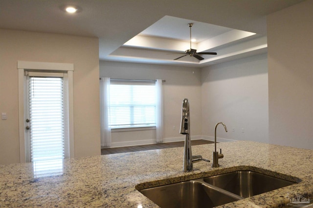 kitchen featuring light stone counters, a tray ceiling, ceiling fan, hardwood / wood-style flooring, and sink