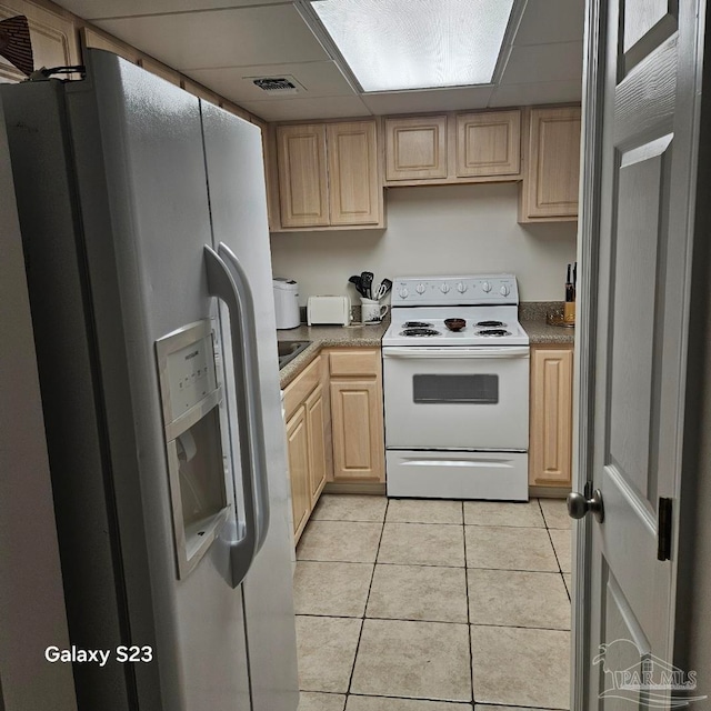 kitchen with light tile patterned flooring, white appliances, and light brown cabinets