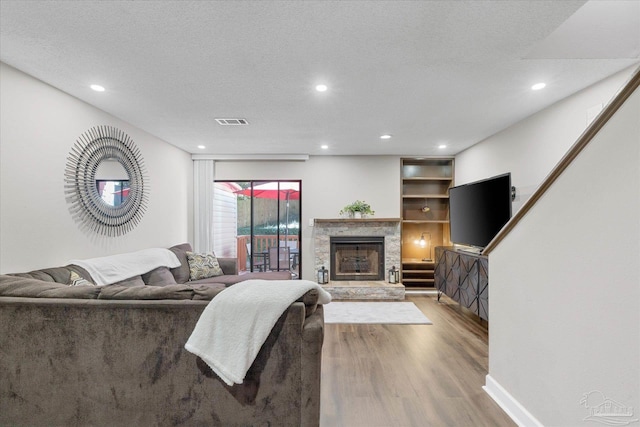 living room with a textured ceiling, a stone fireplace, and light hardwood / wood-style flooring