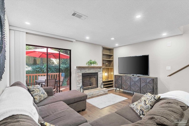 living room with a stone fireplace, a textured ceiling, and hardwood / wood-style floors