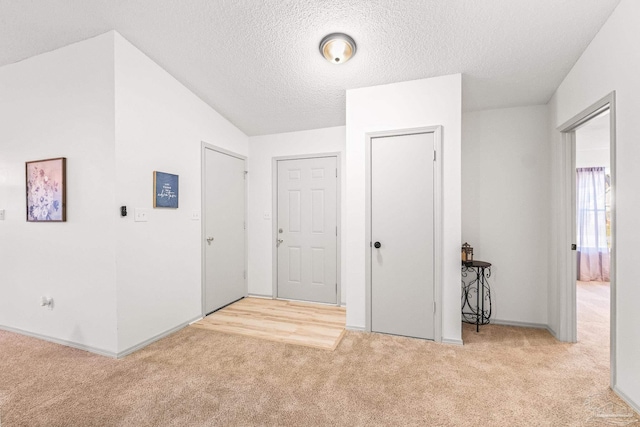 entryway with a textured ceiling, light carpet, and vaulted ceiling