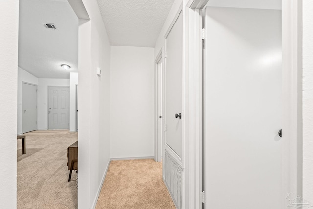 hallway with a textured ceiling and light colored carpet