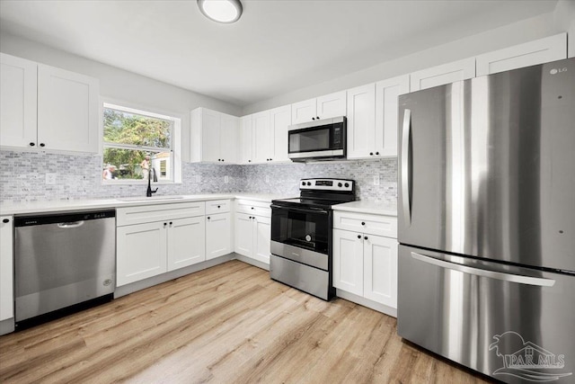 kitchen featuring appliances with stainless steel finishes, light hardwood / wood-style flooring, white cabinetry, and backsplash