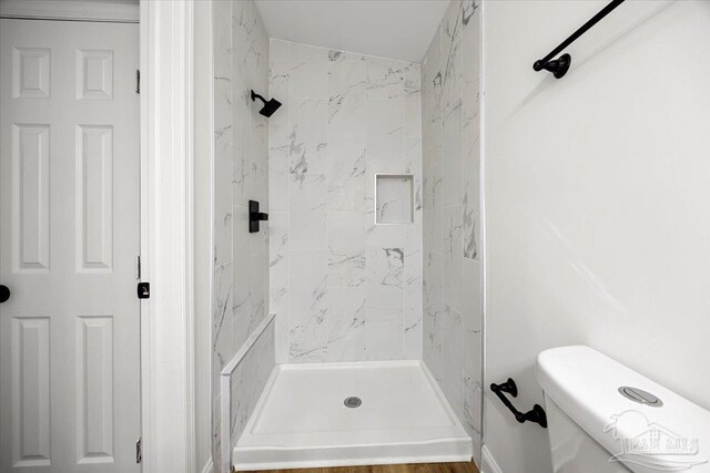 bathroom featuring hardwood / wood-style floors, toilet, and a tile shower