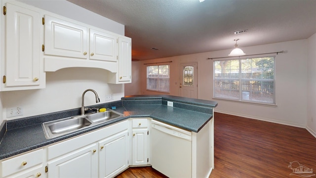 kitchen with dark countertops, white cabinets, white dishwasher, a sink, and a peninsula