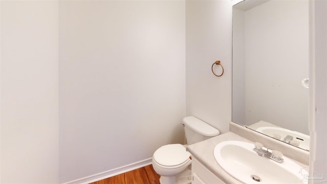 half bathroom with toilet, baseboards, wood finished floors, and vanity