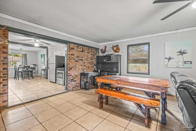 tiled dining space with ceiling fan and crown molding