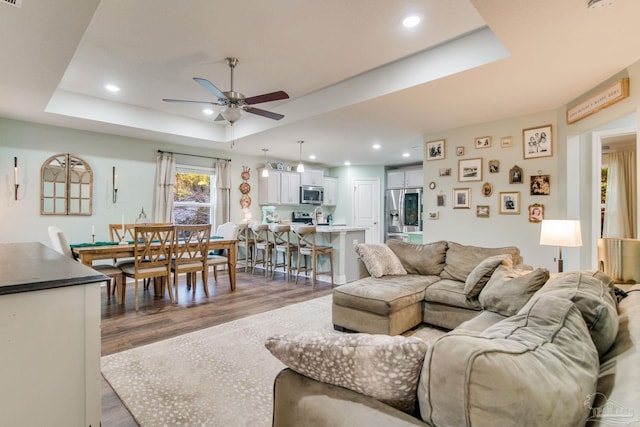 living room with a tray ceiling, ceiling fan, and hardwood / wood-style floors