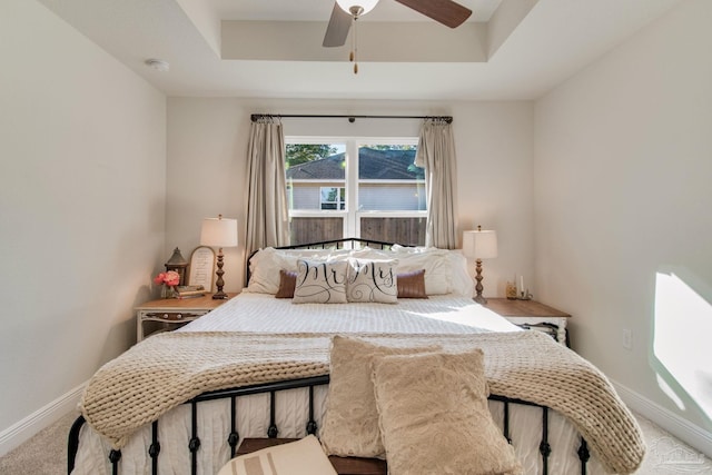 bedroom with light colored carpet, a raised ceiling, and ceiling fan