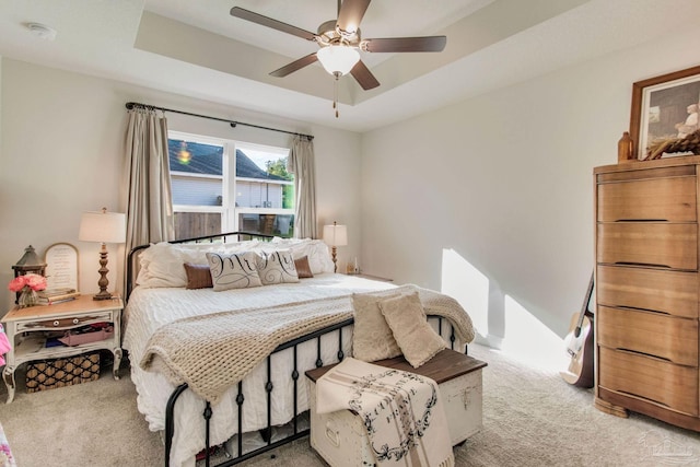 carpeted bedroom with a tray ceiling and ceiling fan