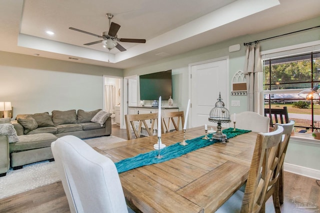 dining space featuring hardwood / wood-style flooring, ceiling fan, and a tray ceiling