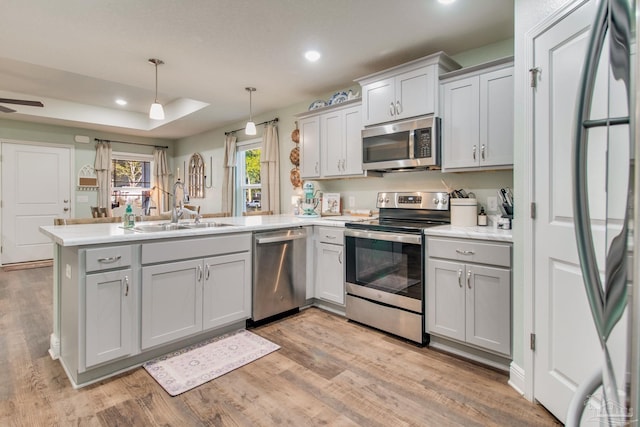 kitchen featuring sink, stainless steel appliances, kitchen peninsula, pendant lighting, and light hardwood / wood-style floors