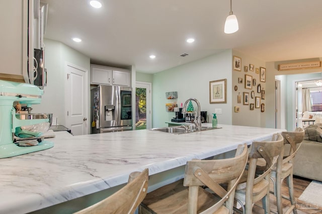 kitchen featuring decorative light fixtures, a kitchen bar, stainless steel fridge with ice dispenser, and sink