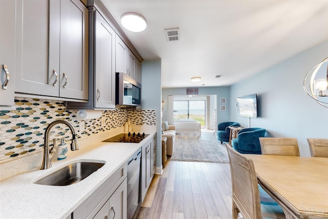 kitchen with tasteful backsplash, sink, light stone counters, light wood-type flooring, and black electric cooktop