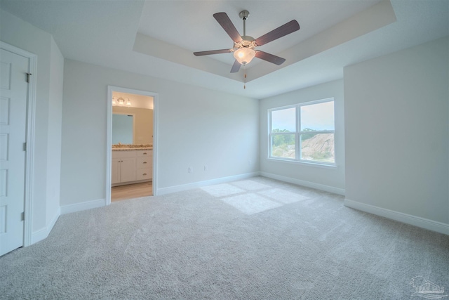 unfurnished bedroom with ensuite bath, light colored carpet, ceiling fan, and a tray ceiling