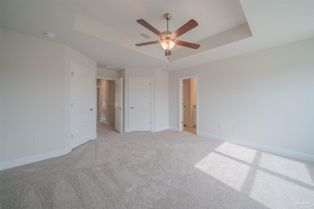 unfurnished bedroom featuring ceiling fan, a tray ceiling, and light carpet