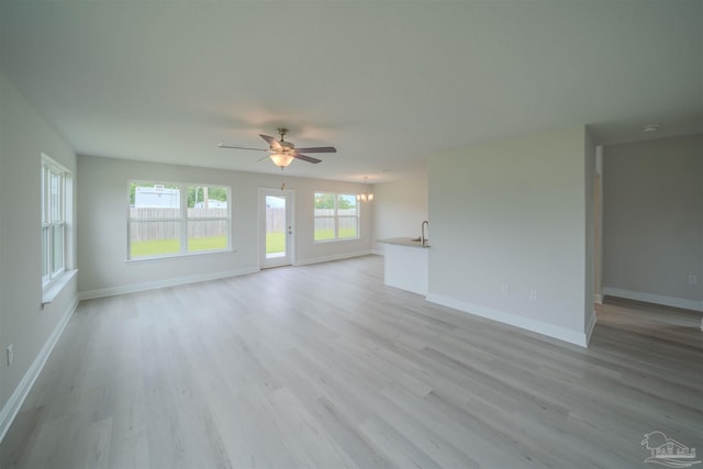 unfurnished living room featuring sink, ceiling fan with notable chandelier, and light wood-type flooring