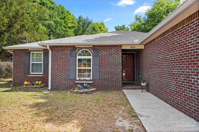 entrance to property featuring brick siding and a yard