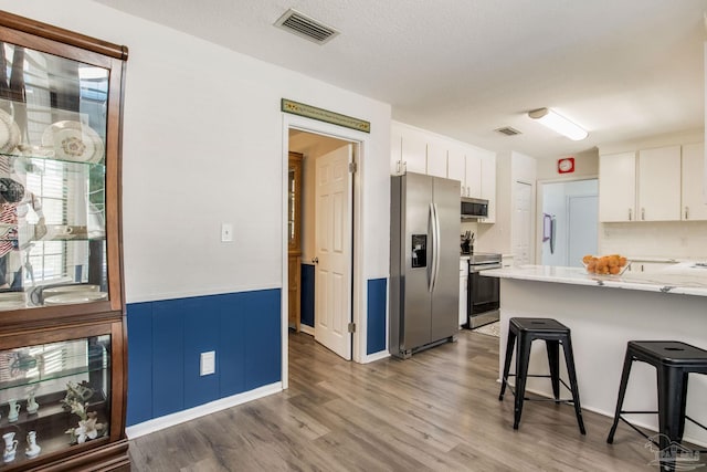 5945 Pamela Dr, Milton, FL 32570 - kitchen featuring appliances with stainless steel finishes, a kitchen bar, white cabinets, wood finished floors, and wainscoting
