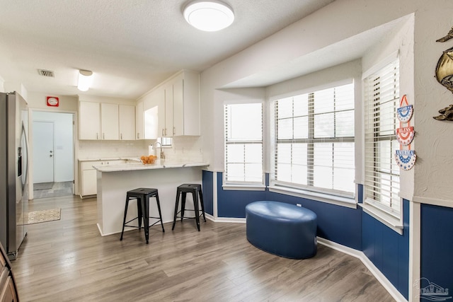 5945 Pamela Dr, Milton, FL 32570 - kitchen featuring stainless steel fridge with ice dispenser, a peninsula, a breakfast bar area, light wood finished floors, and a textured ceiling